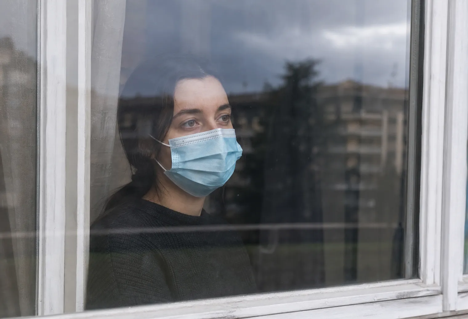 Une personne avec un masque période Covid derrière une fenêtre qui regarde dans